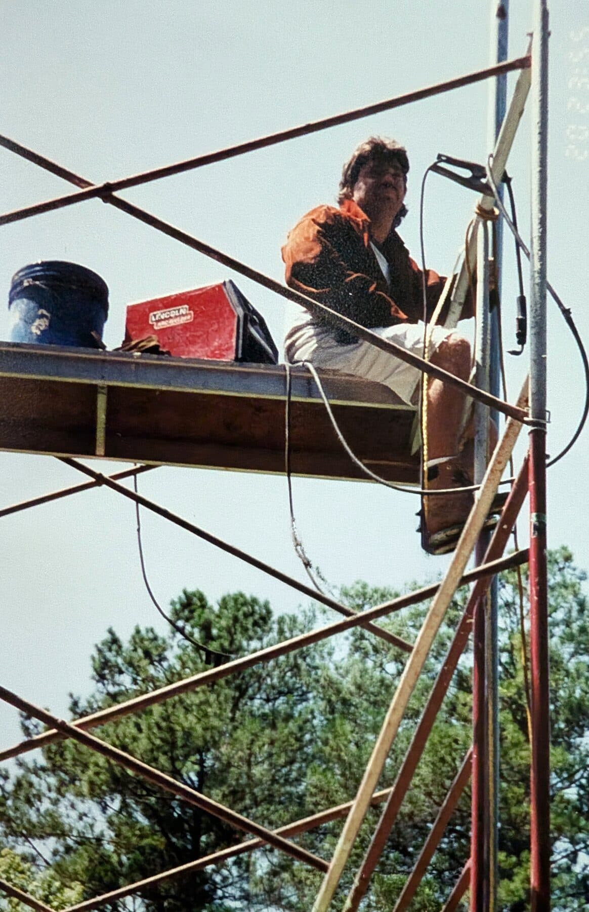 A Country Boy Fence welder on scaffolding, welding steel framing for a community batting cage